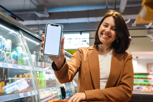 A person is standing in a supermarket aisle, holding up their smartphone. The phone screen displays an AR overlay showing the product's nutritional information and customer reviews. Virtual arrows point towards the product on the shelf.