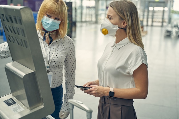 A security checkpoint at a US airport, showing passengers using facial recognition scanners to verify their identity. An officer is standing nearby, monitoring the process. The scene is brightly lit and technologically advanced.
