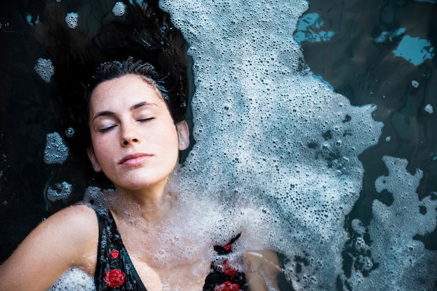 A person taking a cold shower. The water cascading over their body and their facial expression shows a mix of surprise and invigoration. The shower setting is simple and clean, emphasizing the therapeutic aspect of the cold water.