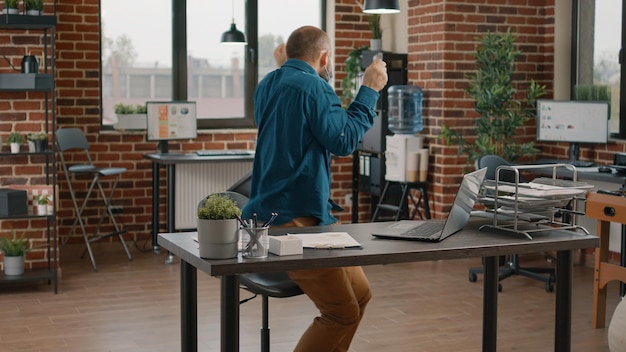 A person using a standing desk in a modern office environment, with colleagues working in the background. The desk is clean and organized, and the person appears focused and energized.