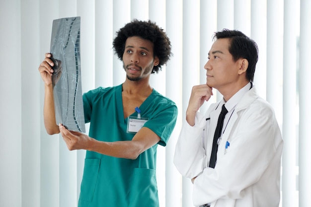 A doctor talking with a patient, the doctor is pointing a model of the human spine while calmly explaining treatment options.