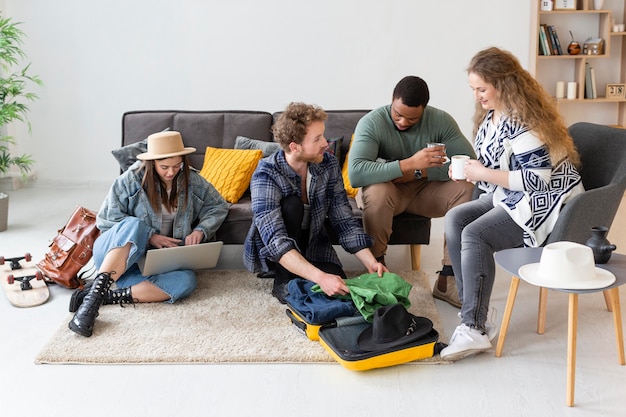 A diverse group of people laughing and talking in the living room of a rented house, with luggage in the background, showcasing the social aspect of the sharing economy.