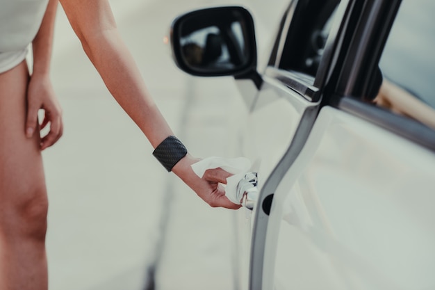 A close-up shot of a person's hands plugging an EV charger into an electric car. The focus is on the connection point and the charging cable. The car is parked inside a home garage and the lighting highlights the charging process.