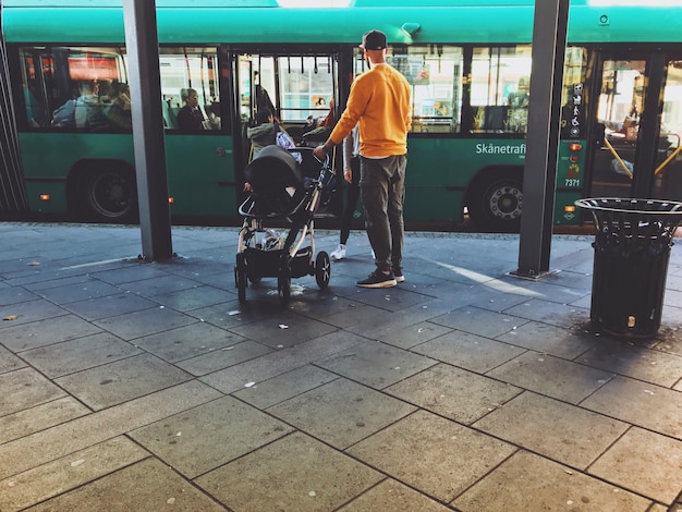 A modern, electric bus pulling up to a bus stop in a bustling city, with diverse people waiting and boarding, showcasing the accessibility and inclusivity of public transportation.