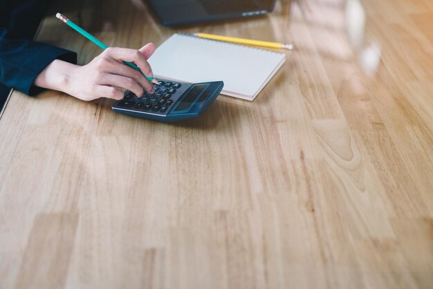A close-up shot of a hand filling out a tax form with a calculator and pen on a wooden desk.